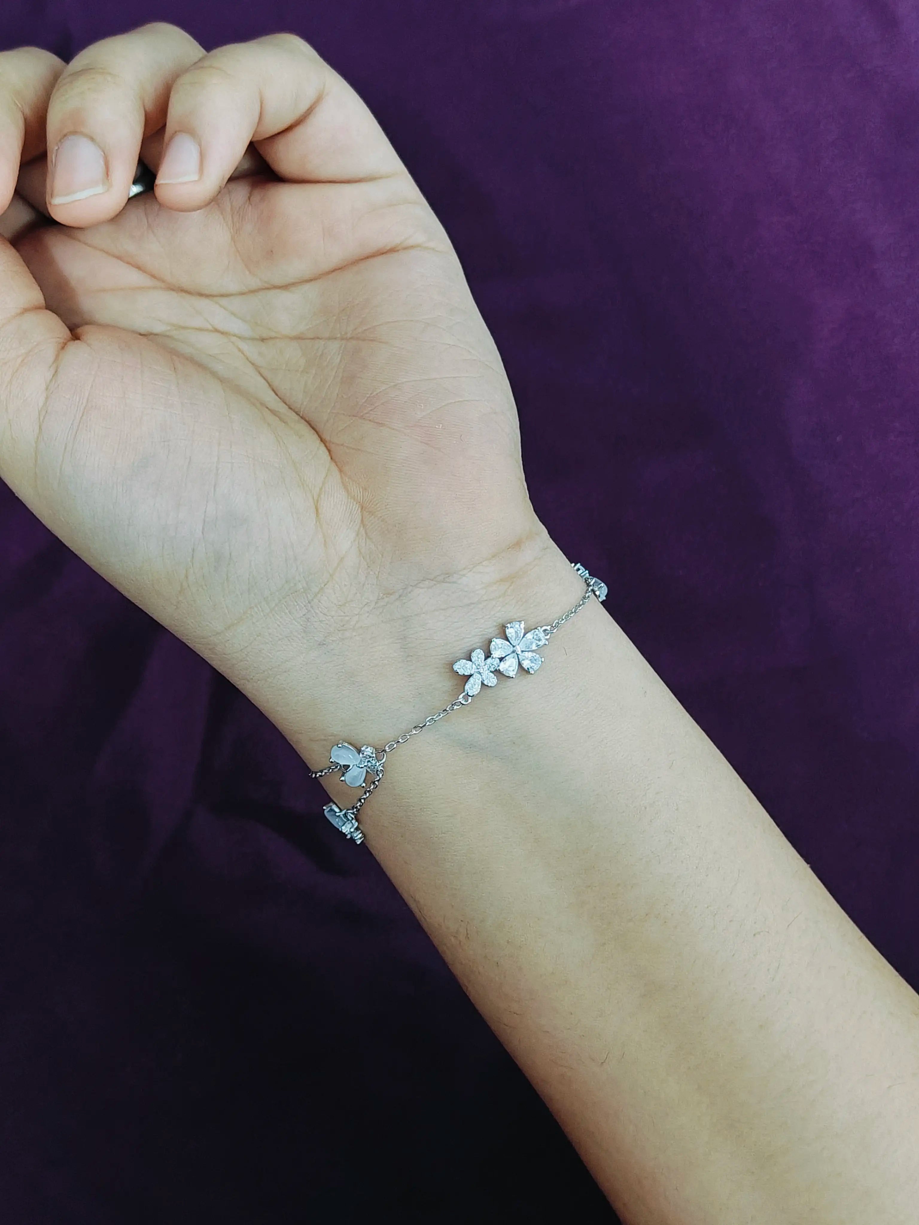 Silver bracelet with floral designs on a wrist against a purple background